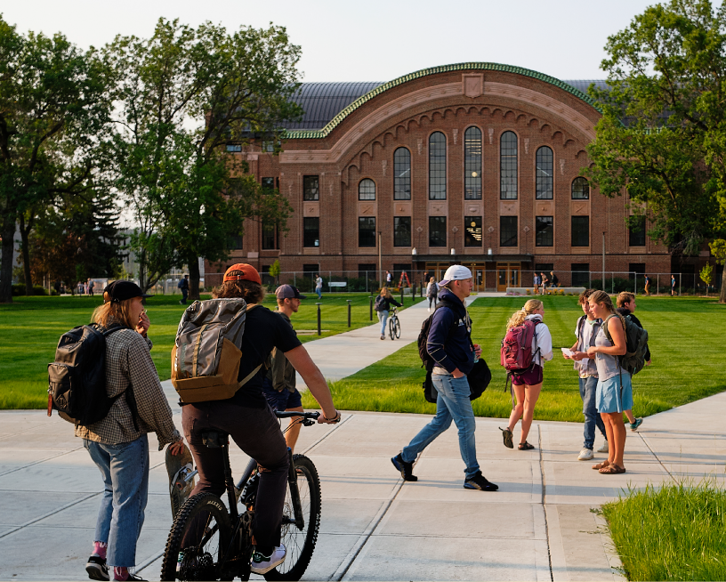 students walking on sidewalks in front of large, older building