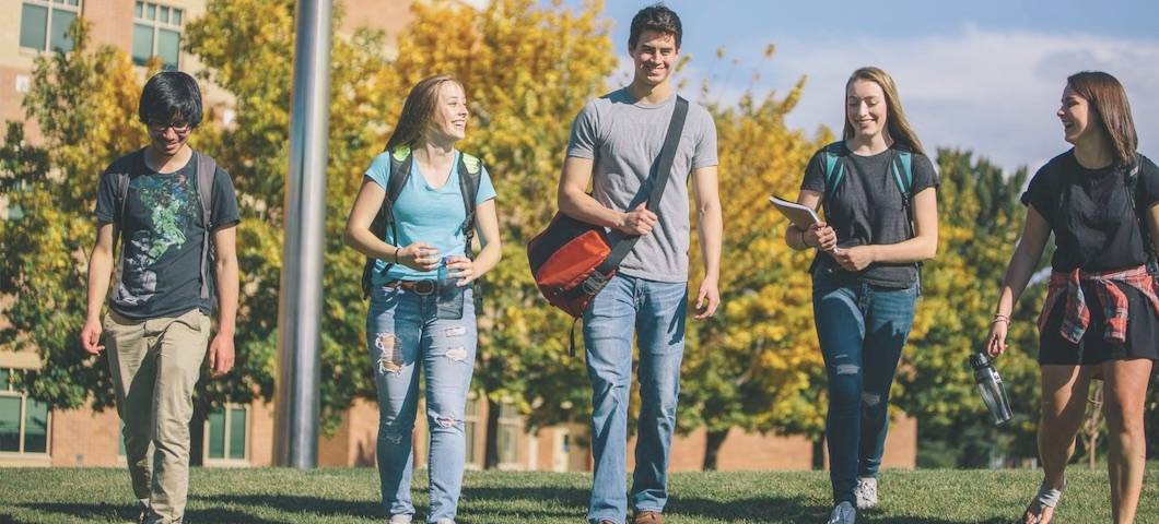 scenic shot of five student walking over grassy knowl