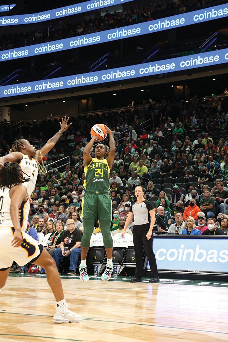 A woman wearing a green and yellow basketball jersey about to shoot the basketball