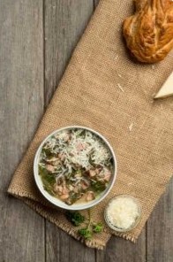 A bowl of Black Eyed Pea and Collard Green soup, topped with cheese.