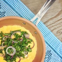 A pan cooking an omelet topped with greens and red onions.