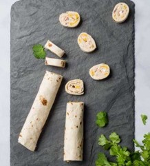 Image of mexican pinwheel slices on a black stone cutting board with cilantro leaves.