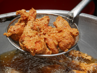 Beef tallow article feature image Crispy fried chicken is being lifted out of a pot of hot cooking oil with a long-handled strainer.
