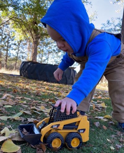 Young child using a toy construction vehicle during outdoor play.