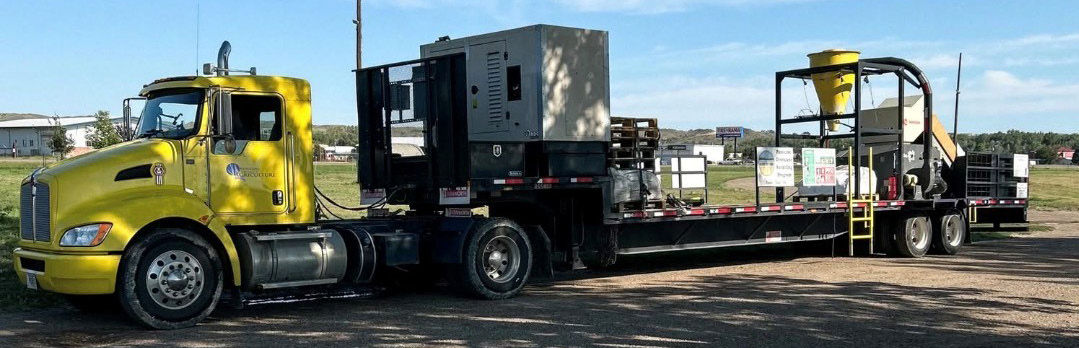 Large truck pulling a trailer equipped with machinery and collection containers for agricultural plastics recycling.