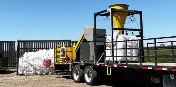 Trailer-mounted agricultural plastics processing equipment parked outdoors beside large bags of collected plastic material.