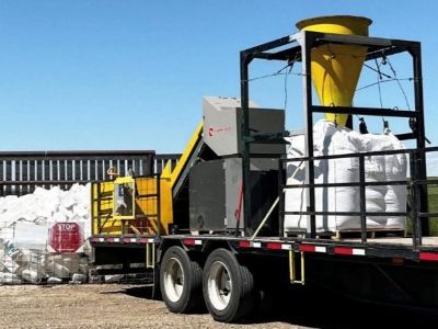 Trailer-mounted agricultural plastics processing equipment parked outdoors beside large bags of collected plastic material.