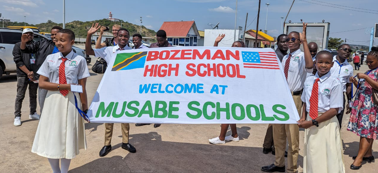 Group of students holding a banner that reads 'Bozeman High School Welcome at Musabe Schools'.
