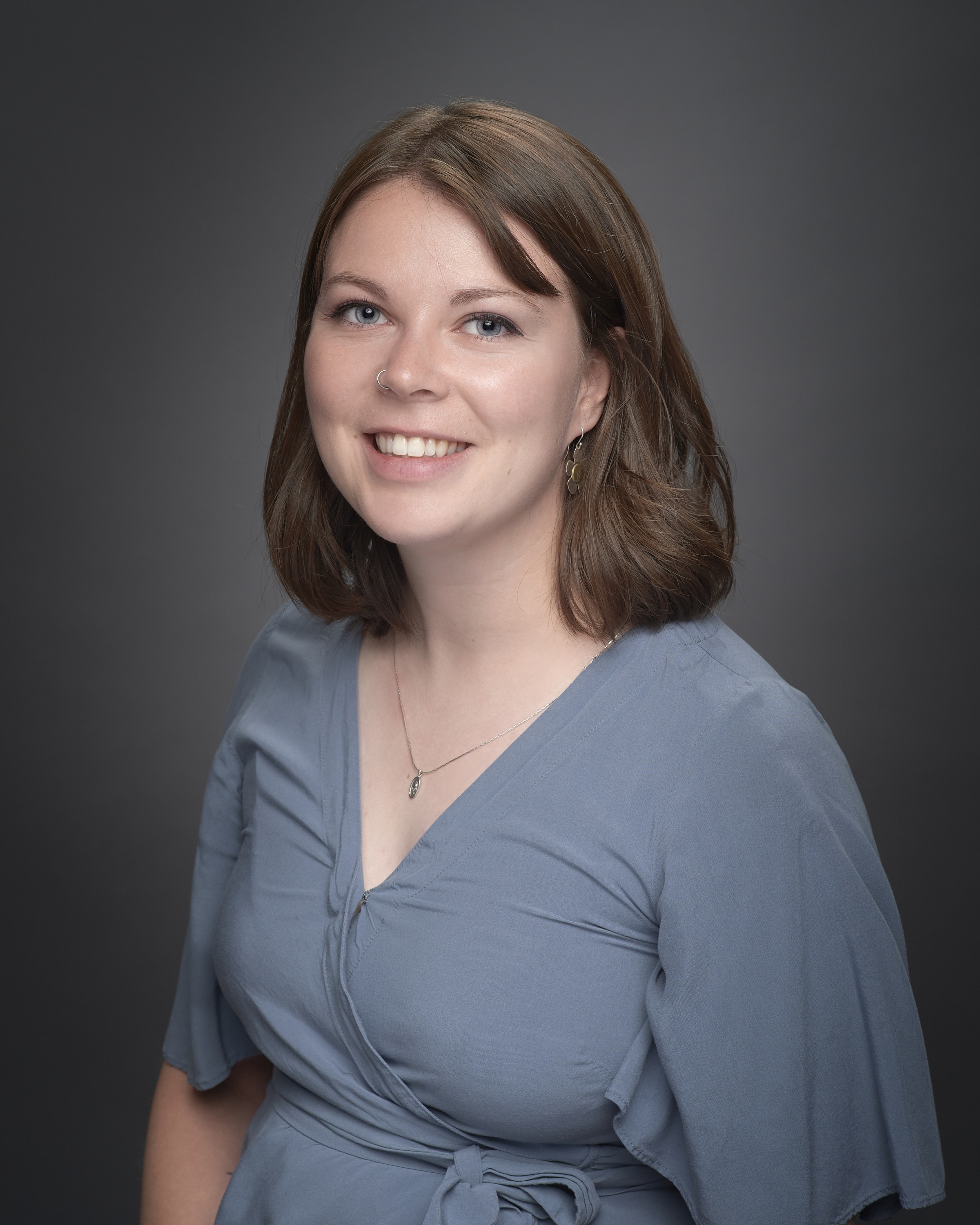 White woman in late 20s with shoulder length brown hair and a blue v-neck shirt