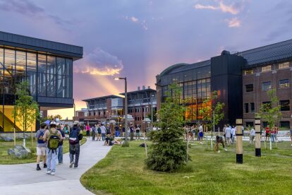 Students walk and gather on a university campus pathway at sunset near modern academic buildings.