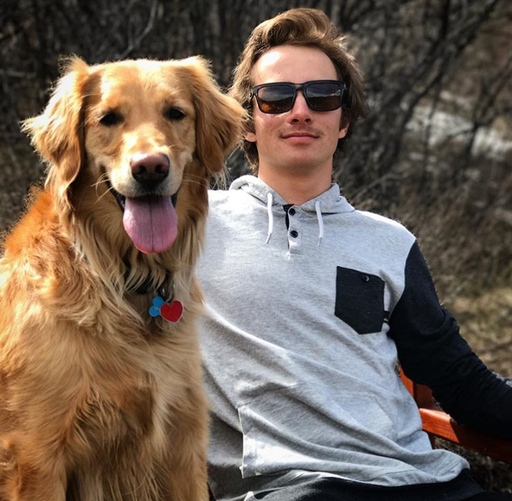Male student wearing sunglasses, sitting with golden retriever